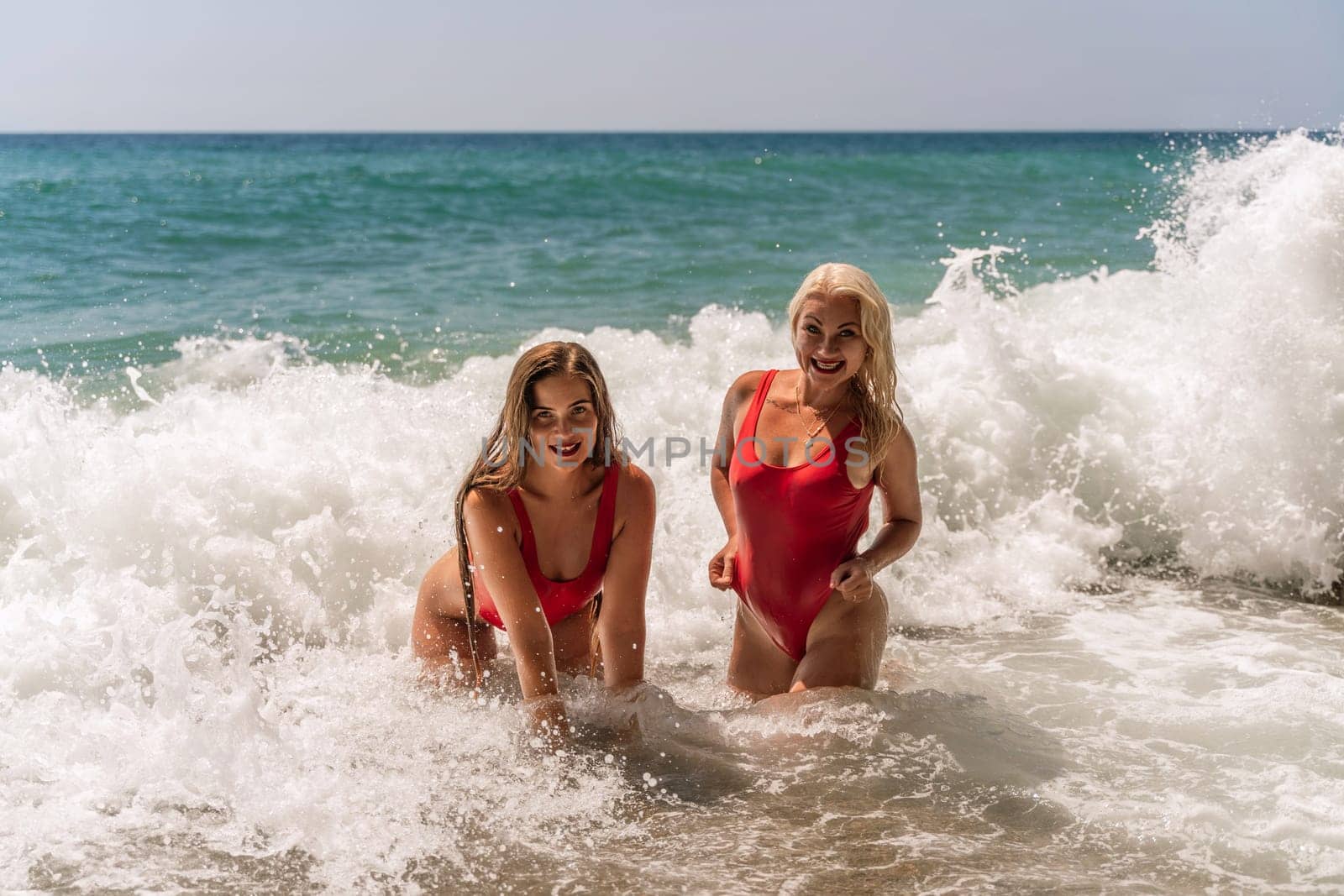 Women ocean play. Seaside, beach daytime, enjoying beach fun. Two women in red swimsuits enjoying themselves in the ocean waves. by Matiunina