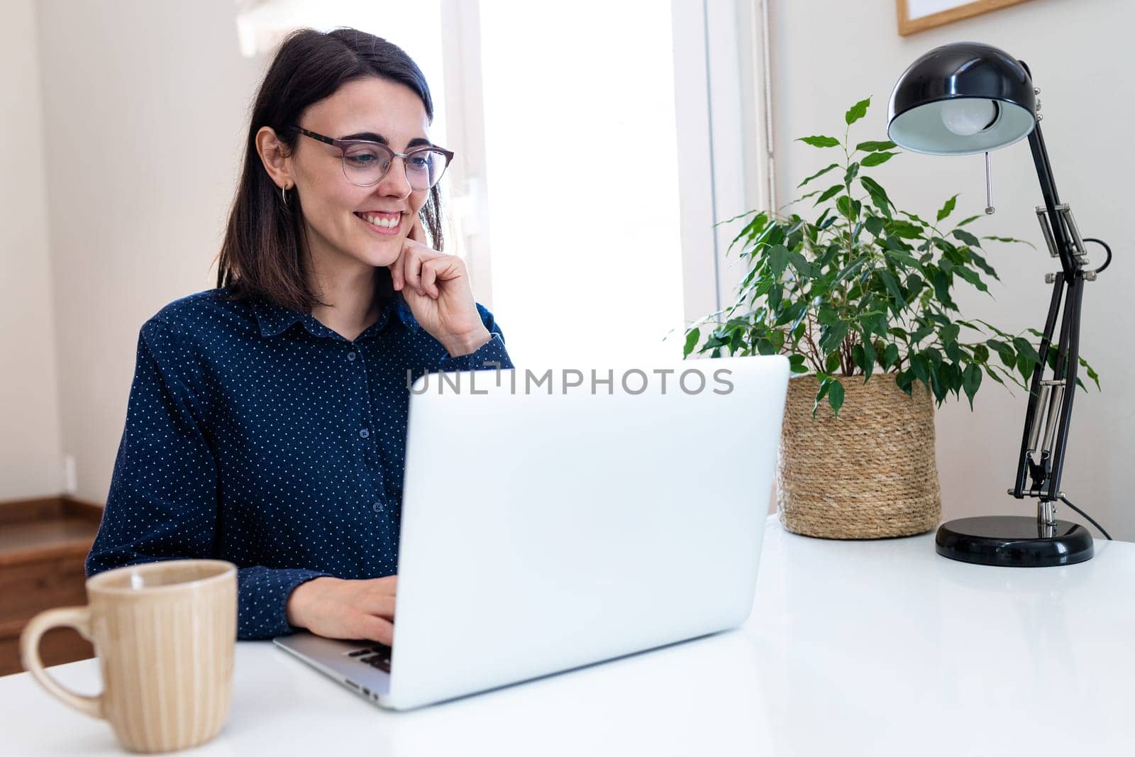 Happy young woman with glasses working with laptop at home. Vertical image. Copy space. by Hoverstock