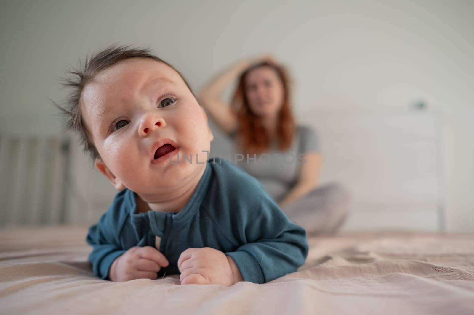 A three-month-old boy lies on his stomach on the bed and his mother sits behind him and cries. Postpartum depression. by mrwed54