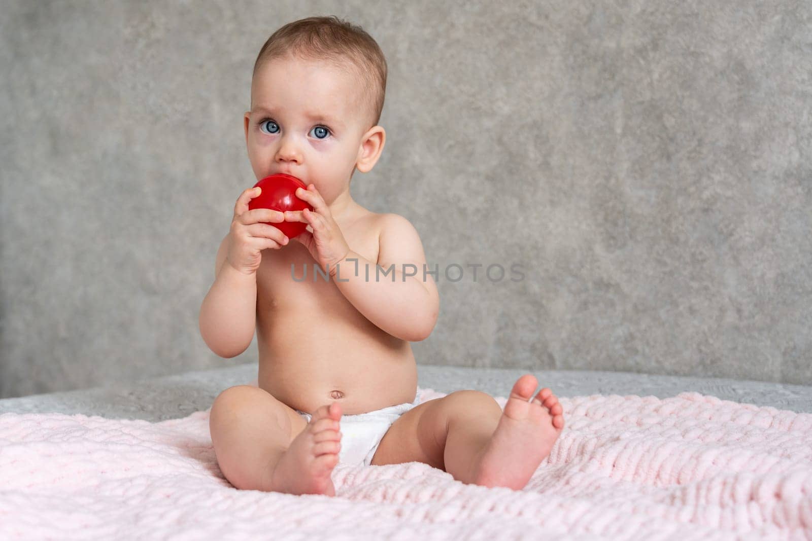 The baby is licking a small toy red ball with concentration.