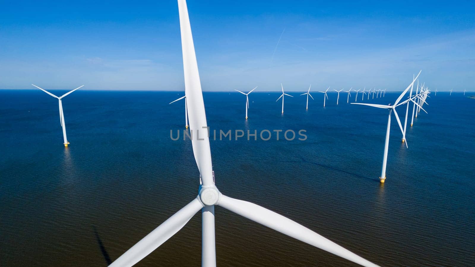 A cluster of wind turbines gracefully harnessing the power of the ocean breeze in the Netherlands Flevoland during a vibrant spring day. drone aerial view of windmill turbines green energy in ocean