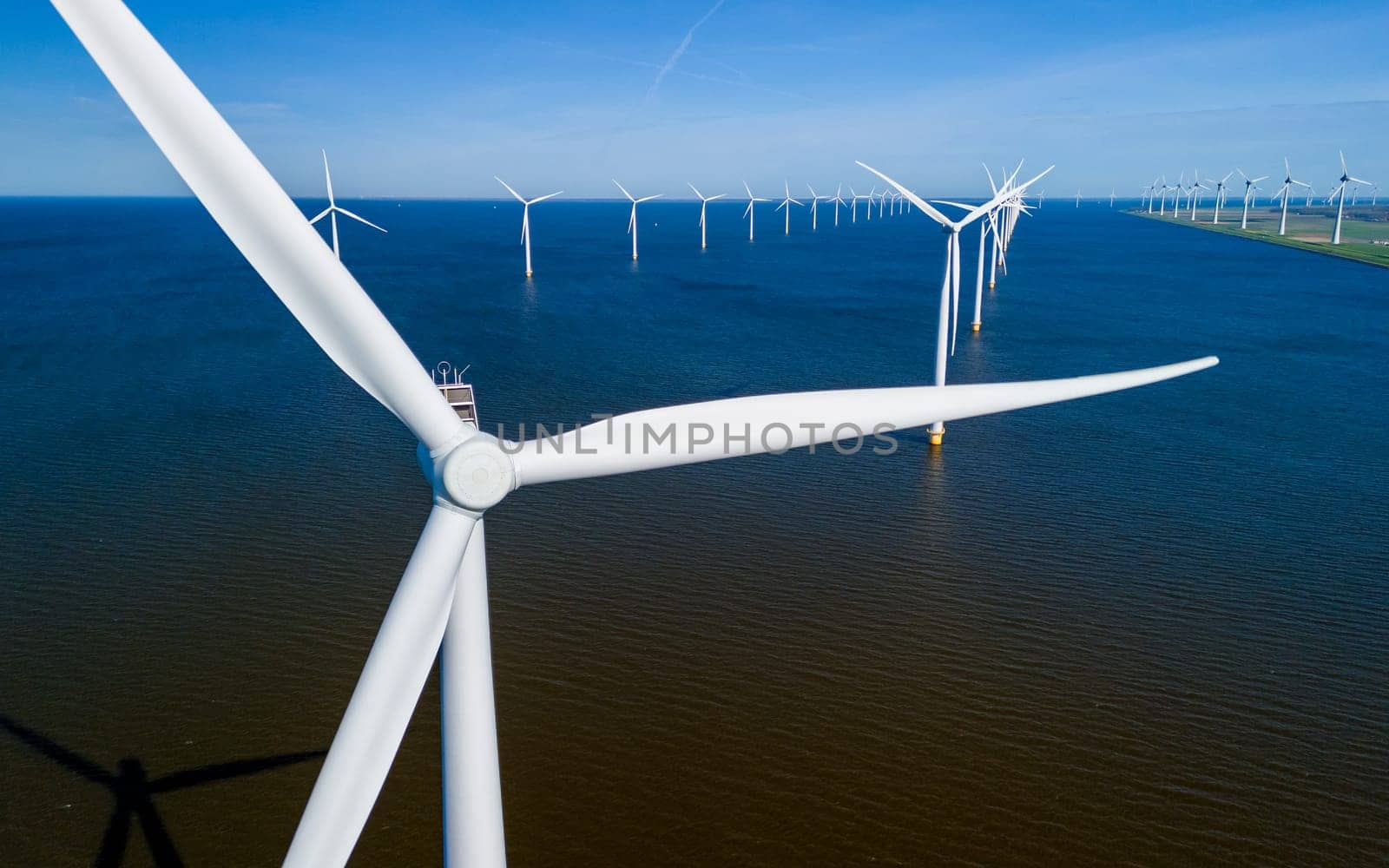 A vast body of water stretches out before the viewer, with numerous windmills standing tall in the background, set against a cloudy sky. windmill turbines in ocean