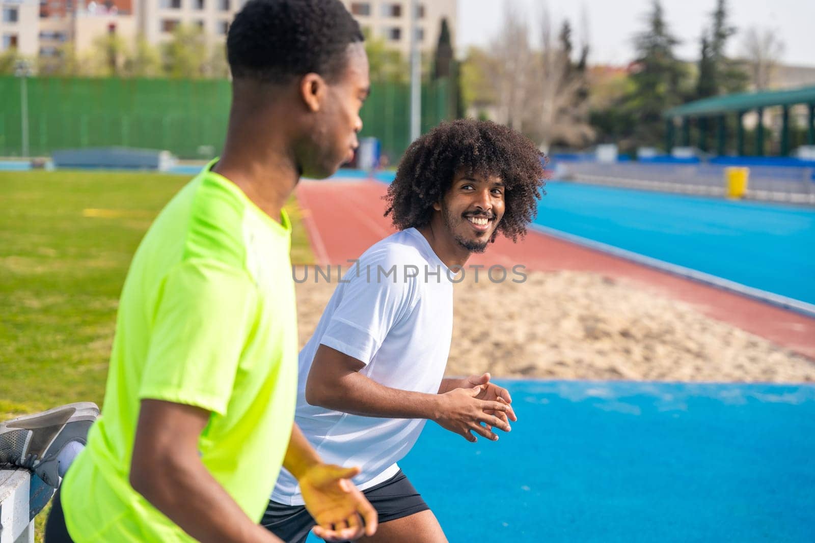 Smiling african young friends warming up in a running track by Huizi