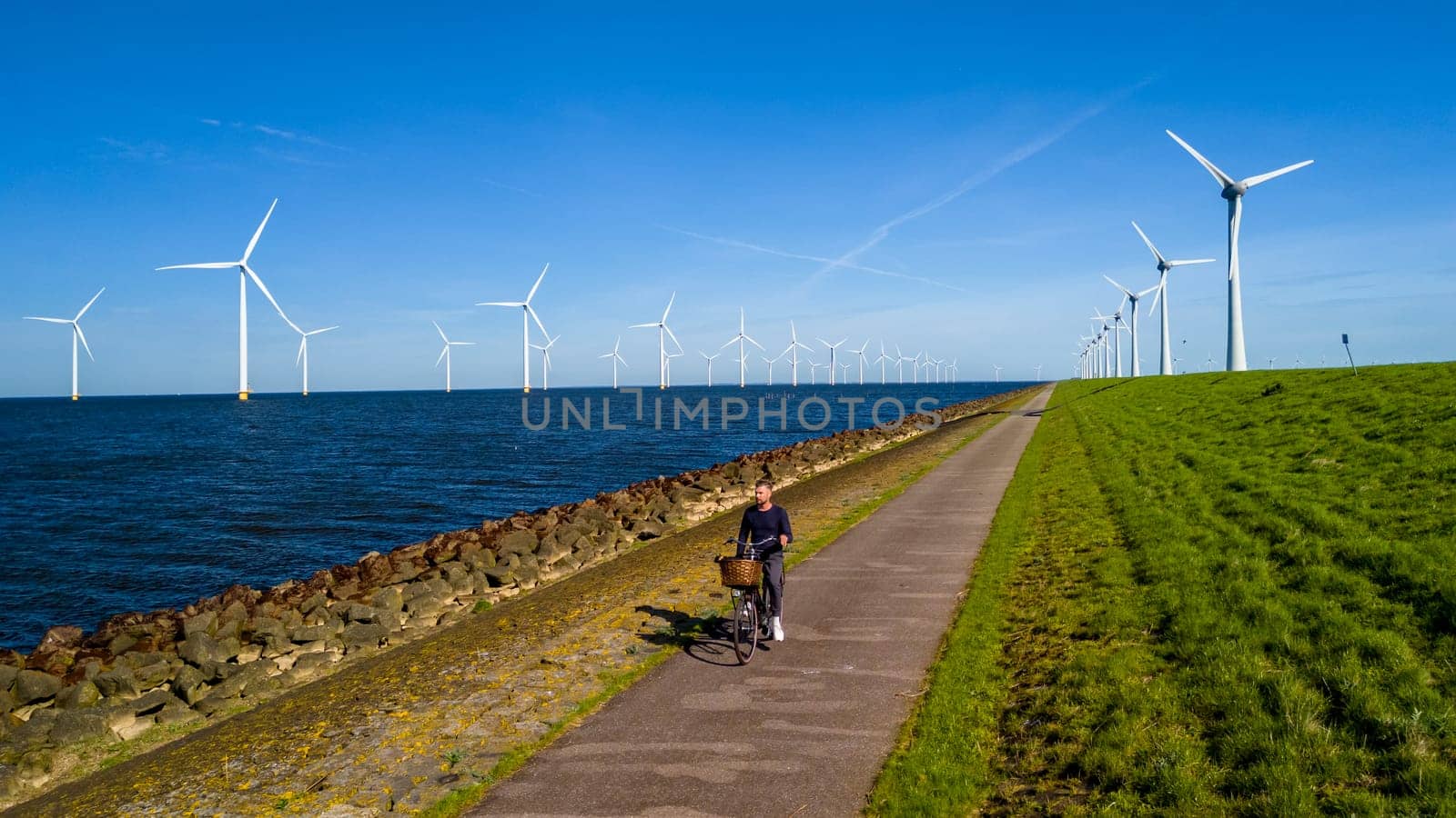 A man elegantly rides a electric bike down a scenic path with windmill turbines in the background by fokkebok