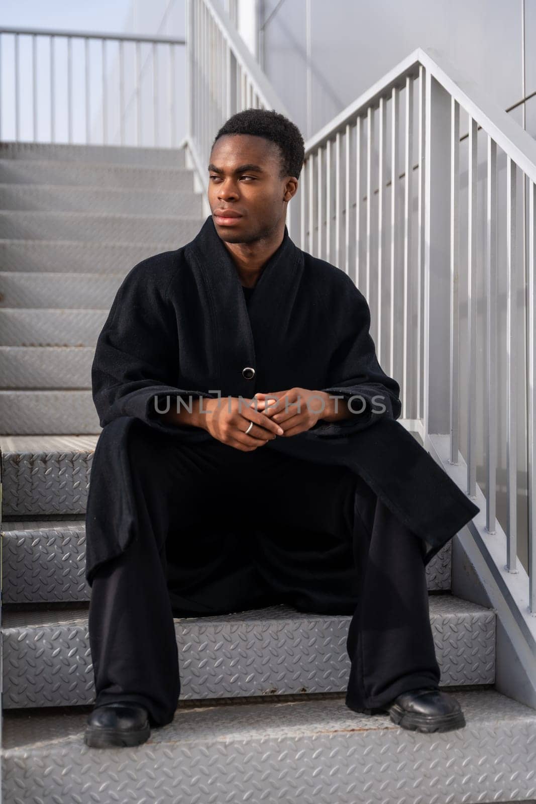 African handsome model sitting on stairs wearing winter black clothes by Huizi