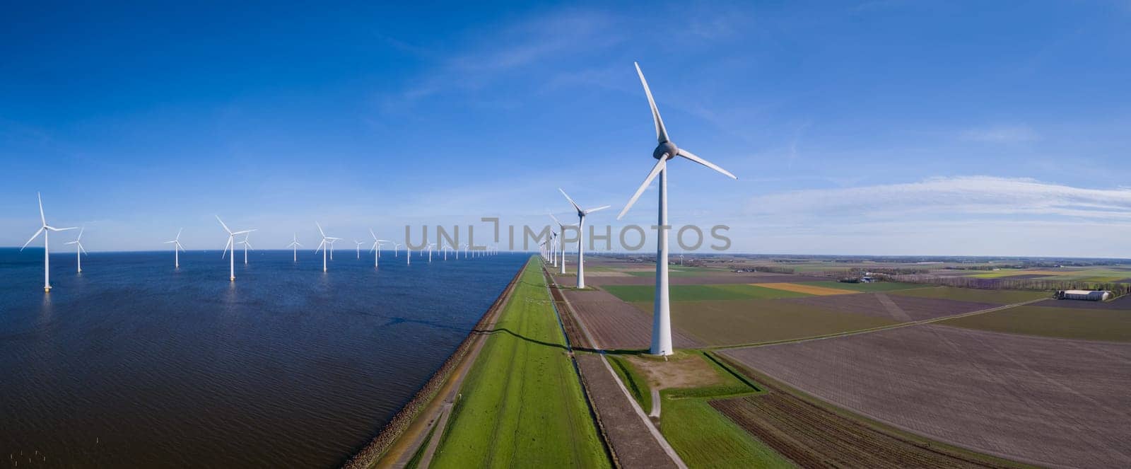 A stunning view of a row of wind turbines gracefully turning along the horizon of a vast body of water in Flevoland, Netherlands during the vibrant season of Spring.