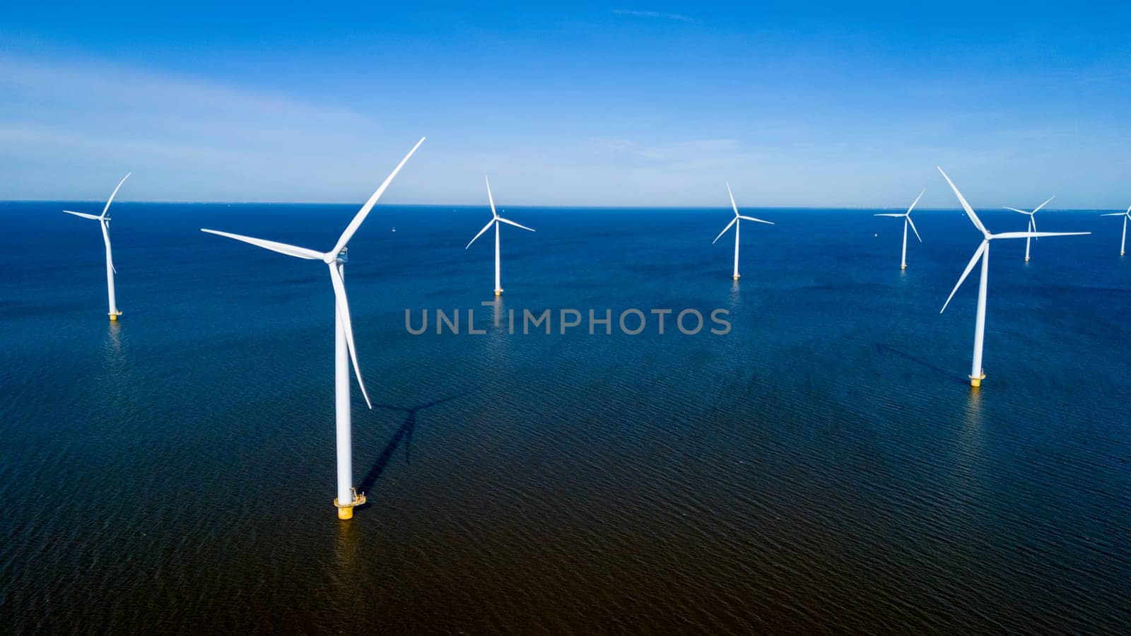 A group of wind turbines elegantly spin in the ocean off the coast of the Netherlands by fokkebok