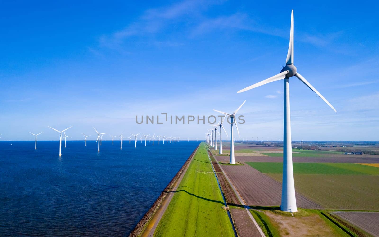 A serene landscape where a row of wind turbines stands tall next to a tranquil body of water in the Netherlands Flevoland during springtime by fokkebok