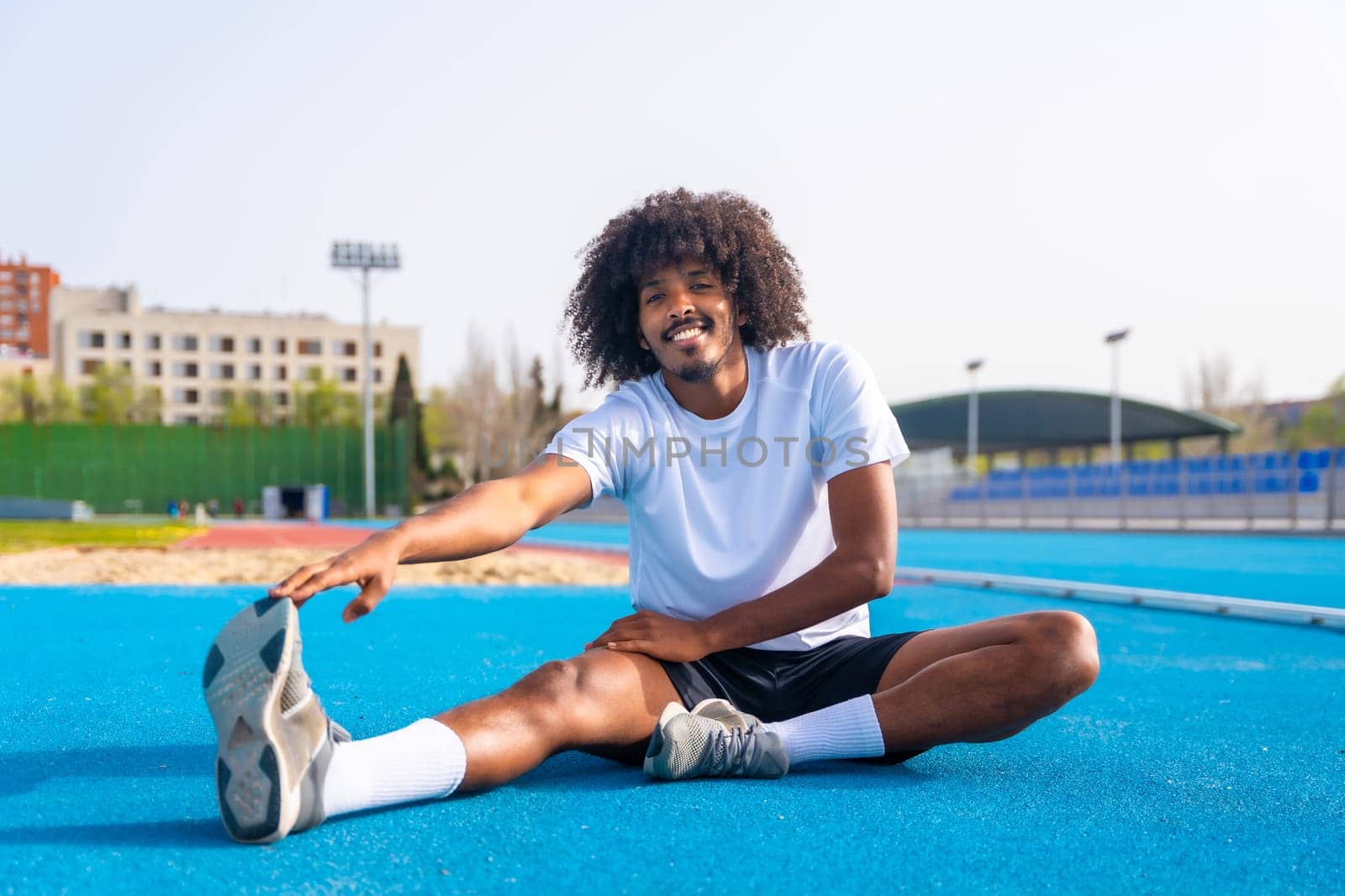 African man stretching in an outdoor running track by Huizi