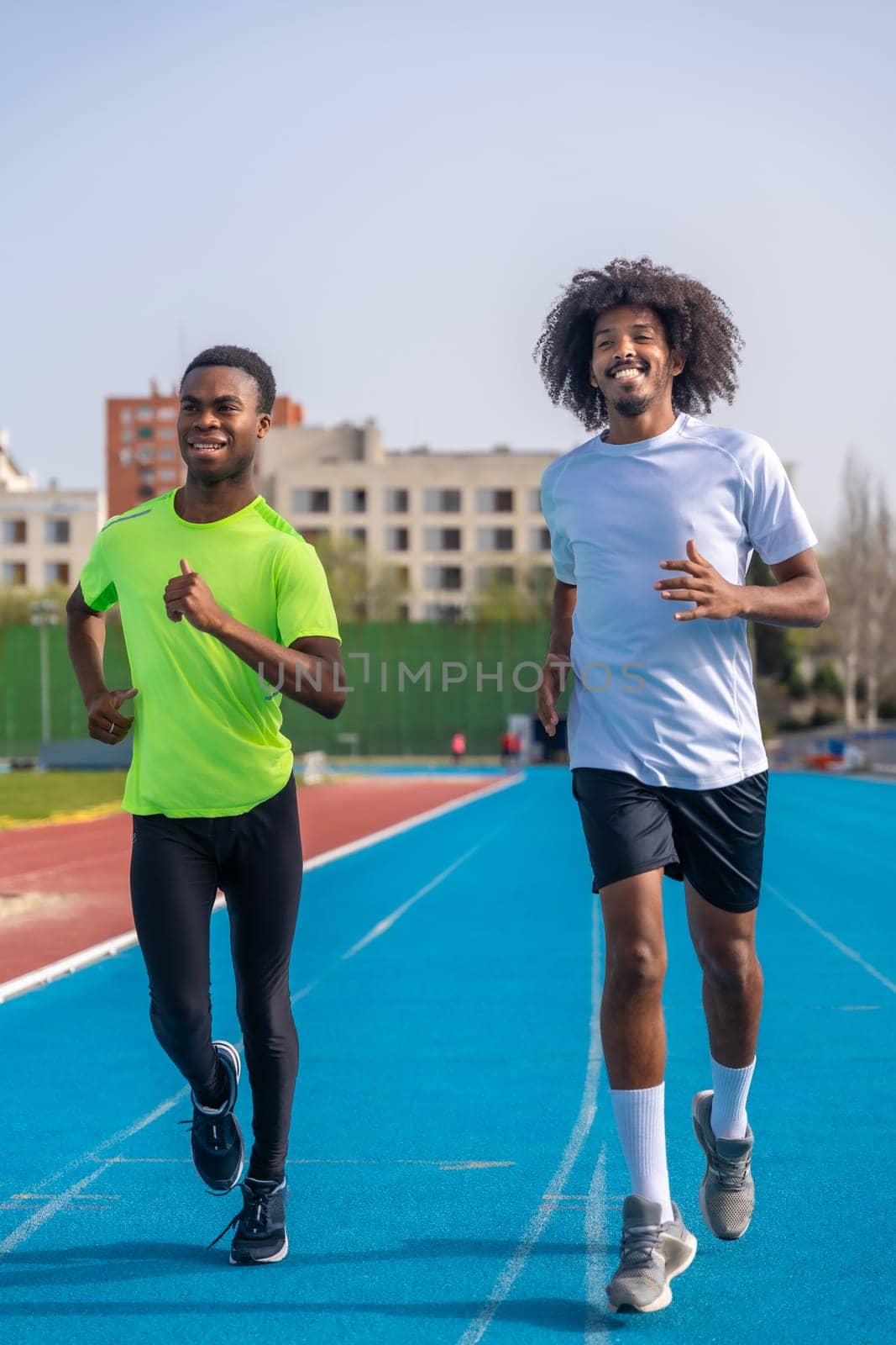 Vertical photo of two african american young ans sportive runners smiling while training together in an outdoor track
