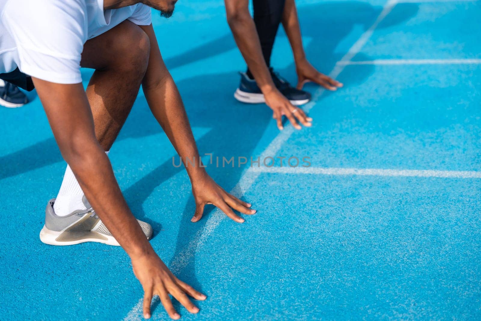 Close-up with copy space of hands of young african males in position to start a race in a blue running track