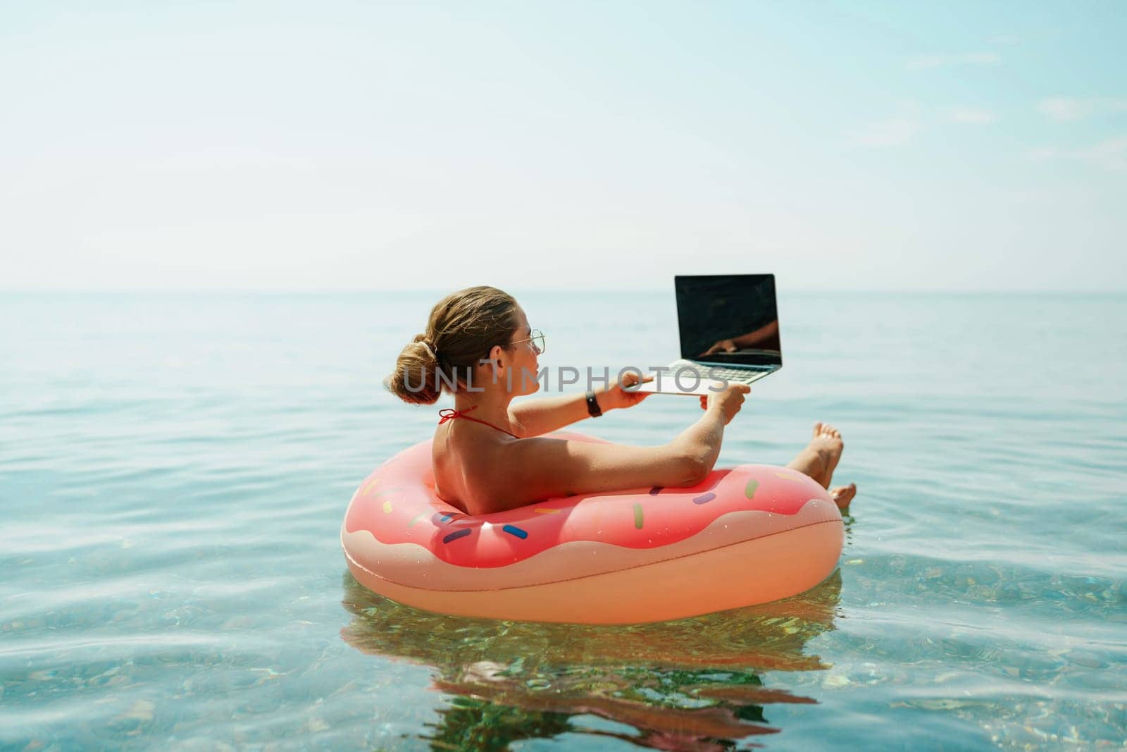 Woman laptop sea. Freelancer woman in sunglases floating on an inflatable big pink donut with a laptop in the sea. People summer vacation rest lifestyle concept