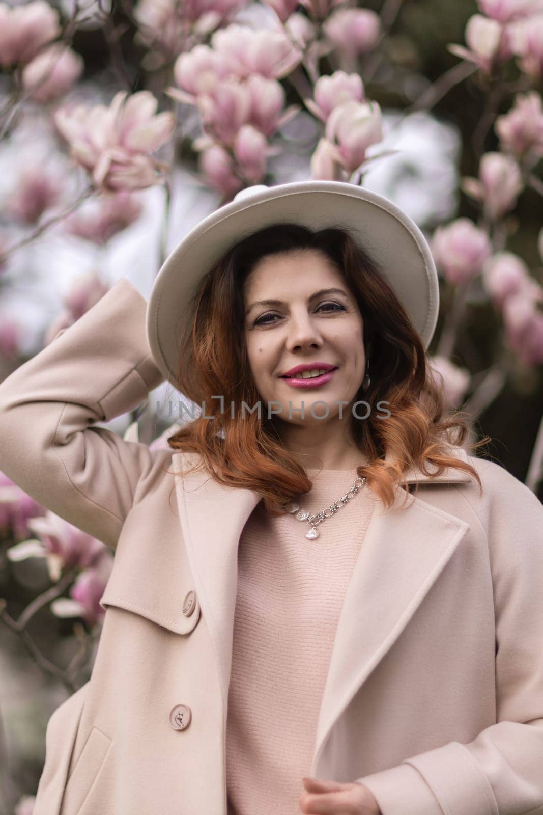 Woman magnolia flowers, surrounded by blossoming trees, hair down, white hat, wearing a light coat. Captured during spring, showcasing natural beauty and seasonal change