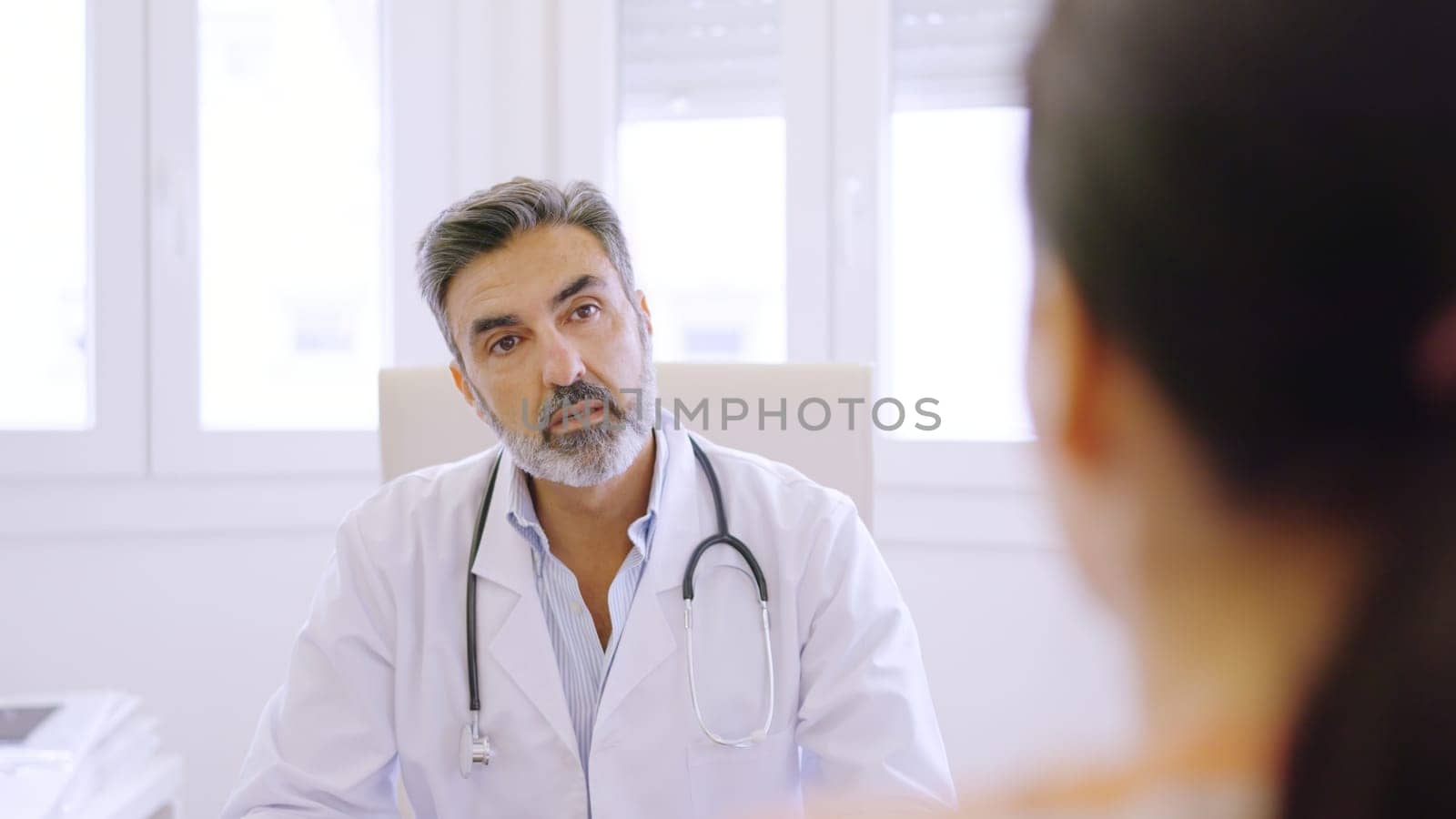 Doctor listening to a female patient in a clinic by ivanmoreno