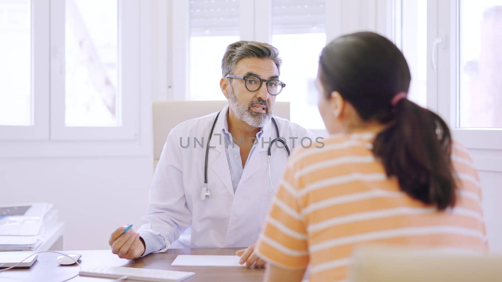 Doctor writing down notes and talking to a woman by ivanmoreno