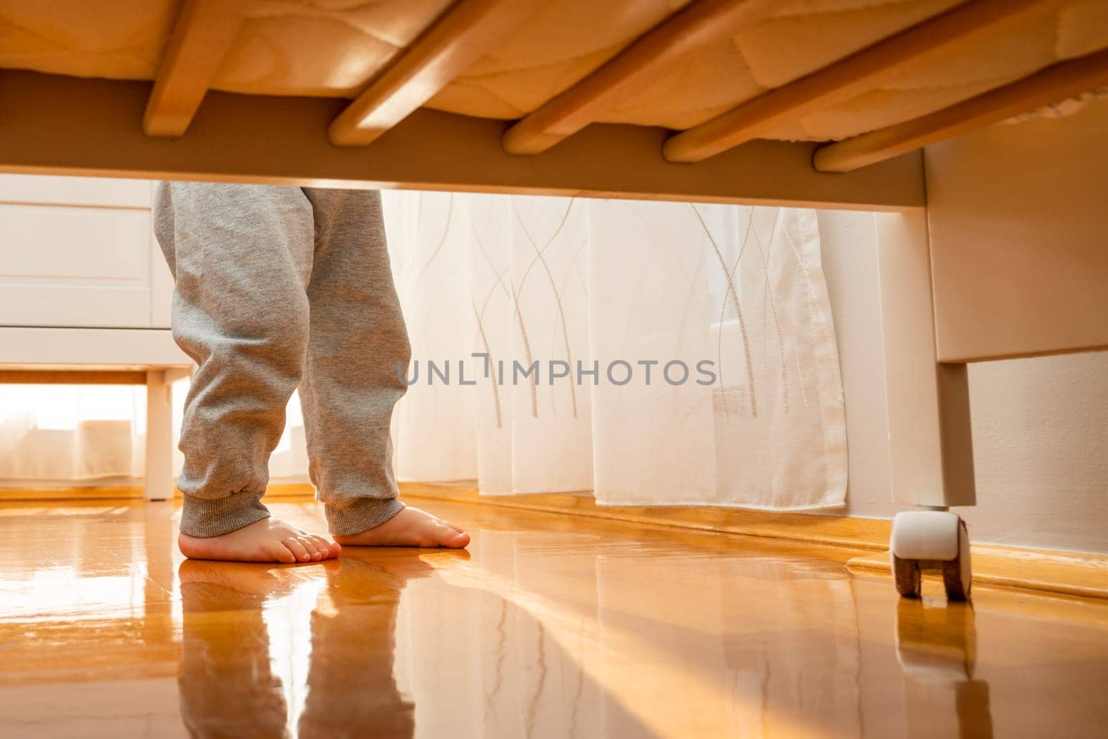 Baby walking barefoot to a crib photographed from the floor. Hidden frame concept.