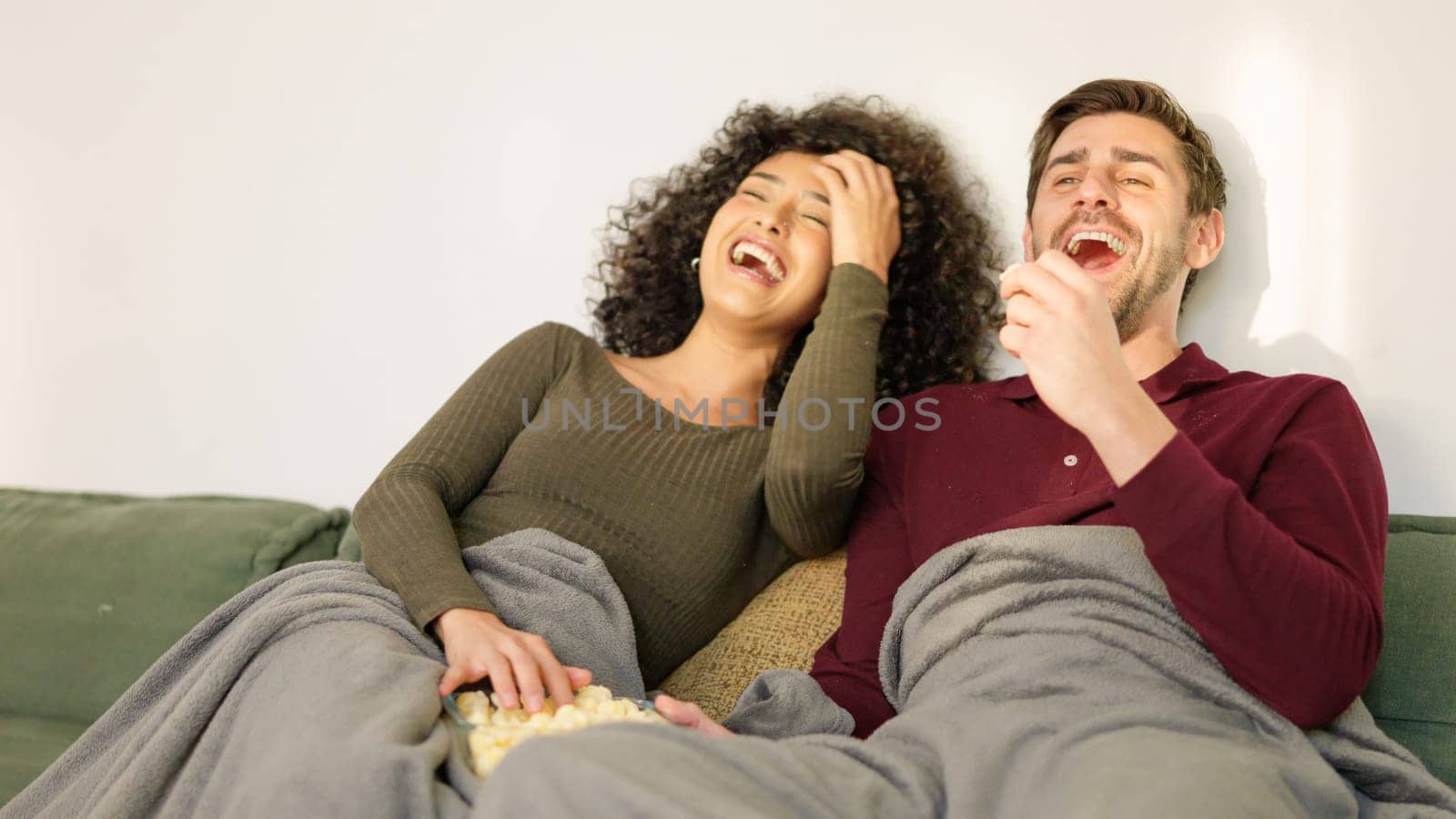 Multiracial couple laughing while watching fun film at home