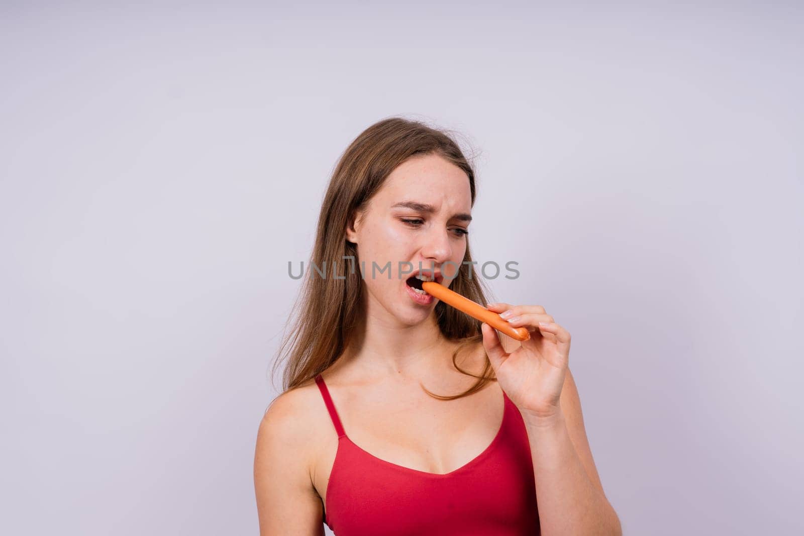 Close-up of a woman eating a sausage. Cropped photo in studio by Zelenin