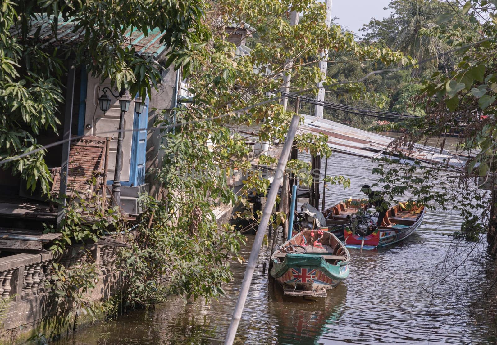 One wooden rowboat and Two small motor boat moored behind house on canal amongst trees and water. Space for text, Selective focus.