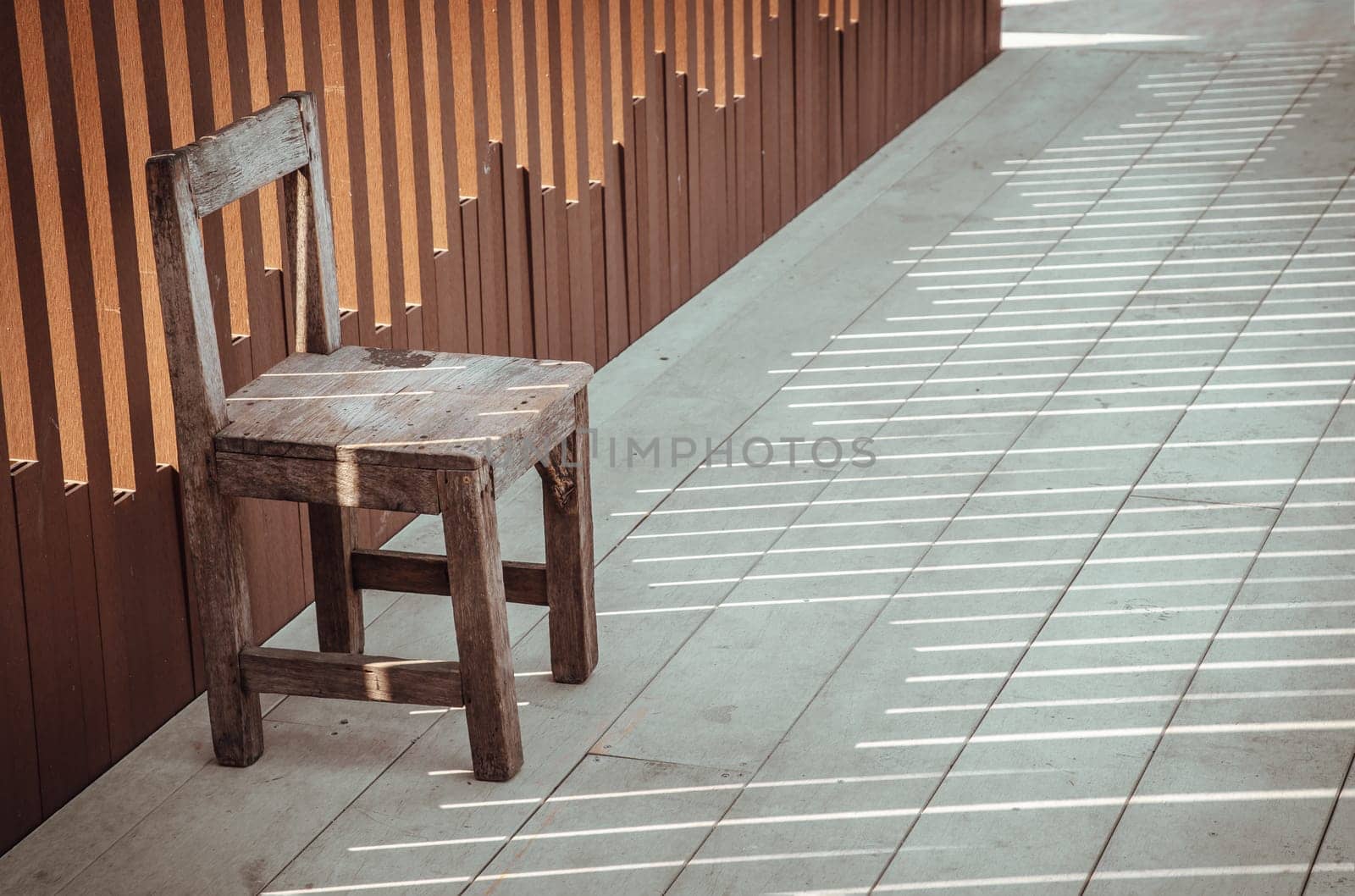 The old wooden chair is in front of the wall, which the sunlight is through it. Relaxing corner in the sunny day with good atmosphere, Copy space, Selective focus.