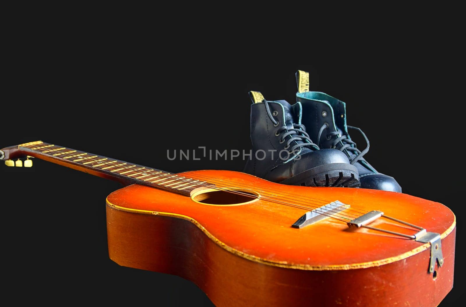 Rock and roll concept. Black boots and acoustic guitar. Rock and roll boots on black background.