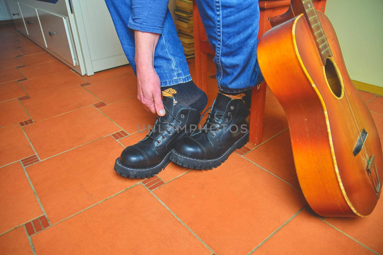 Rock and roll concept. Black boots and acoustic guitar. Putting on rock and roll boots.