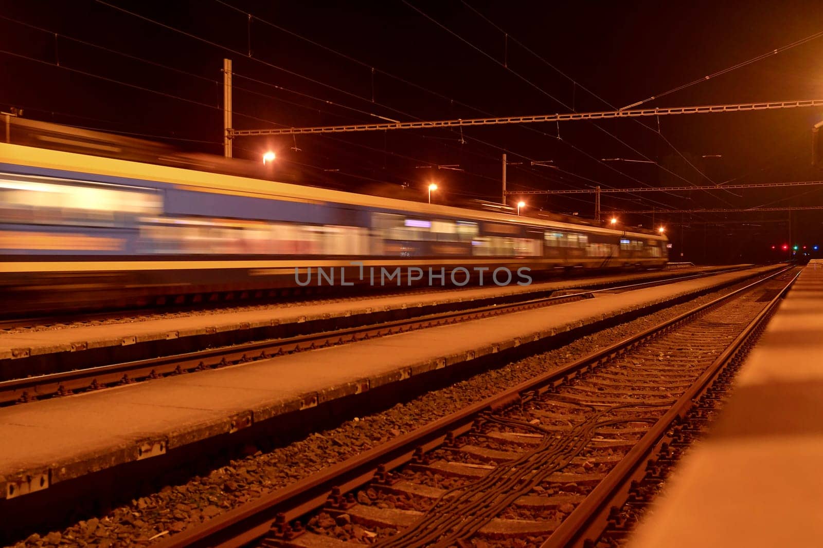 High speed passenger train on tracks with motion blur effect at night. Railway station in the Czech Republic.