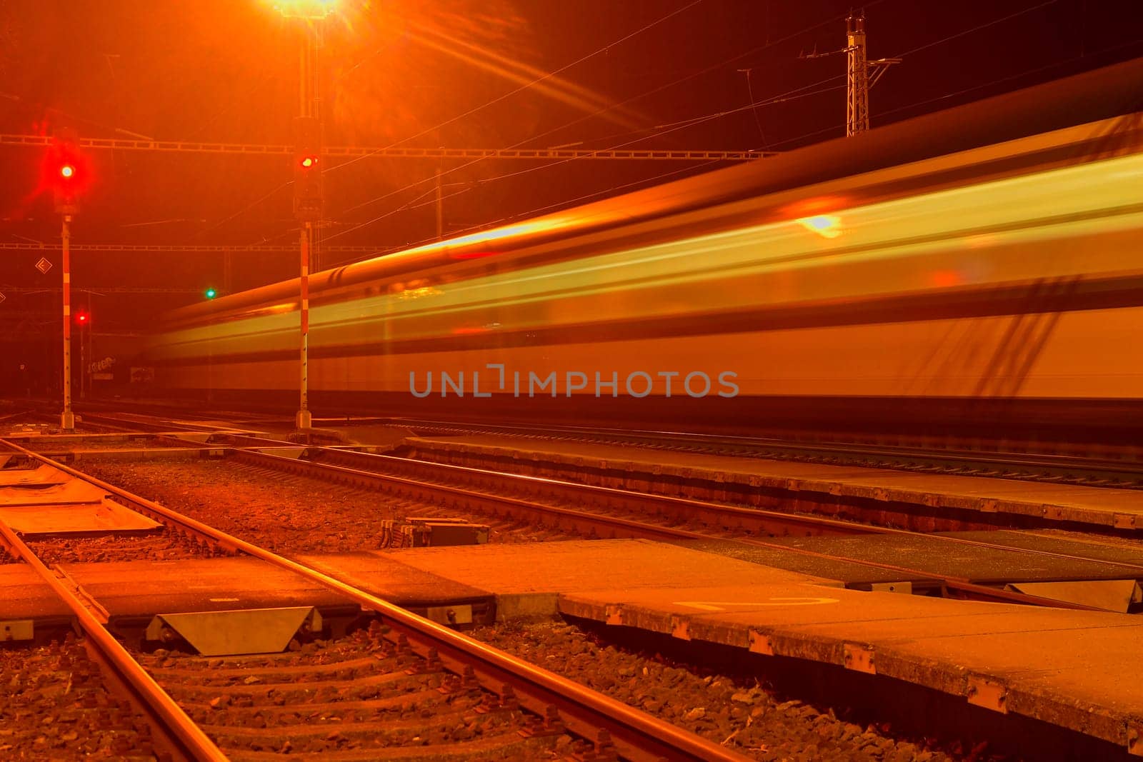 White and blue train passing a small roofless train station at night in the Czech Republic. Blurred motion train.