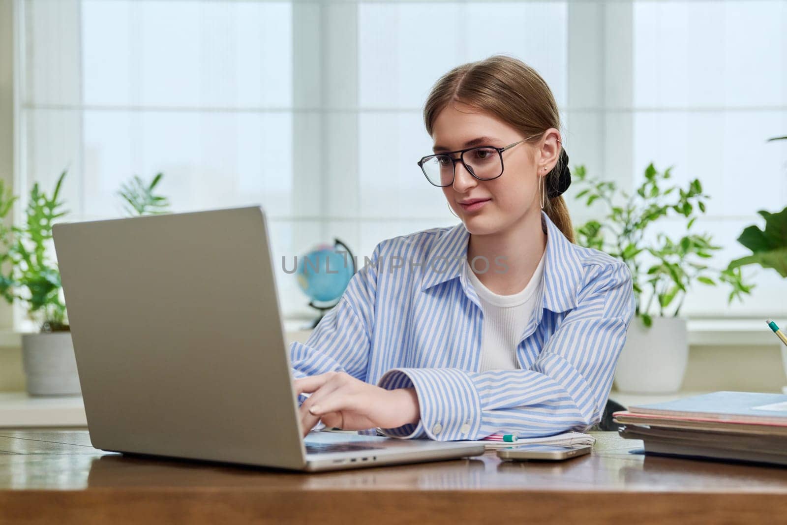 Young smiling female typing on laptop computer at home by VH-studio