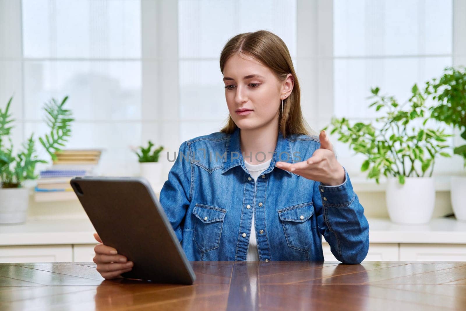 Young teenage female student sitting at home looking talking in web camera of digital tablet. Girl teenager 16,17,18 years old studying remotely, video conference call, e-learning technology education