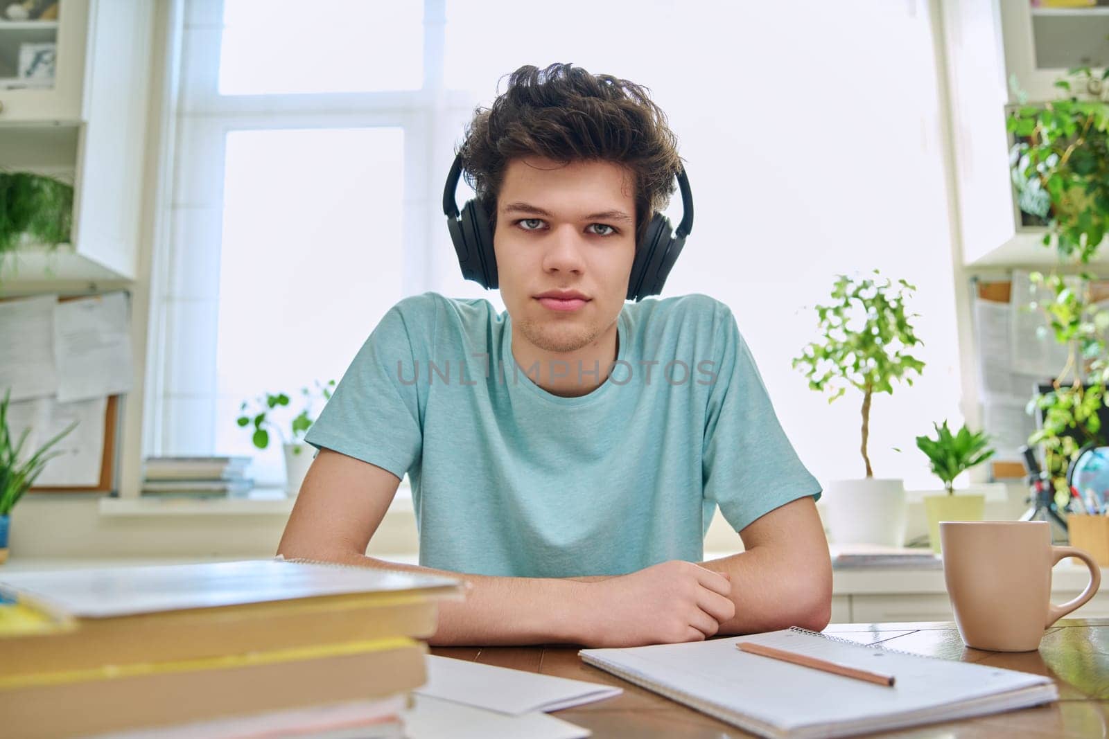 Webcam view of college student guy wearing headphones, talking looking at camera, sitting at desk in home. Young male studying online, video chat call conference, e-learning technology education