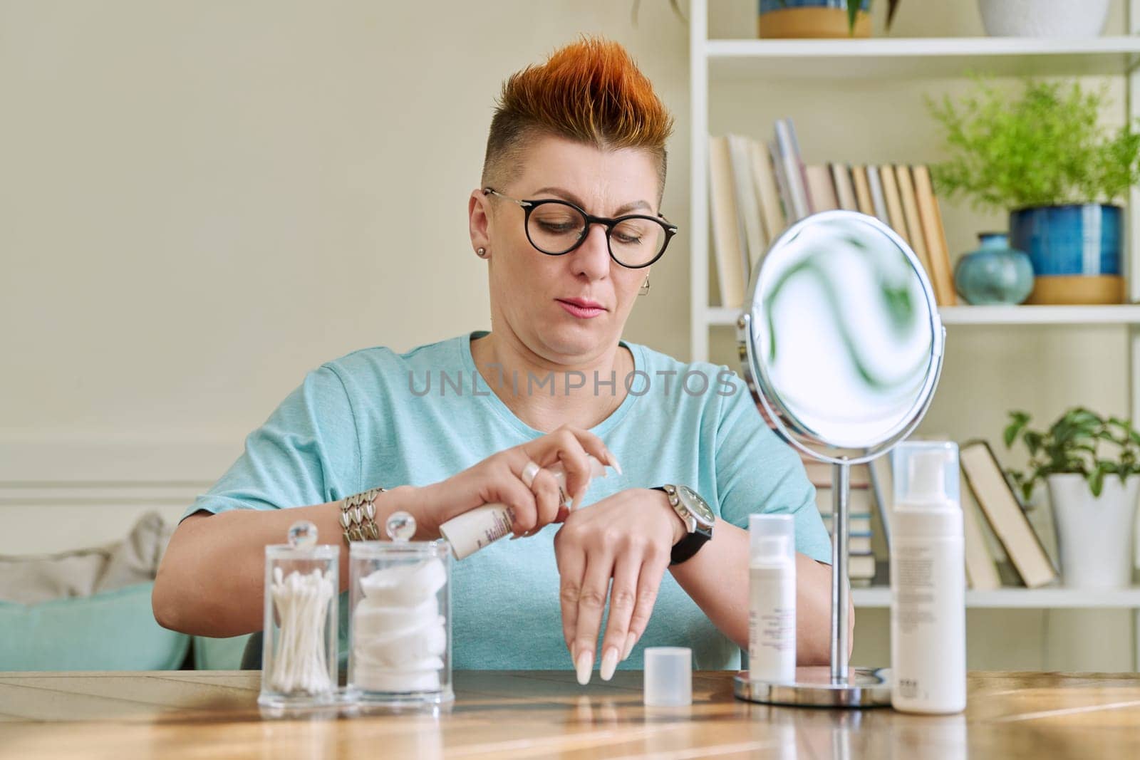 Middle-aged woman with a mirror taking care of her facial skin by VH-studio