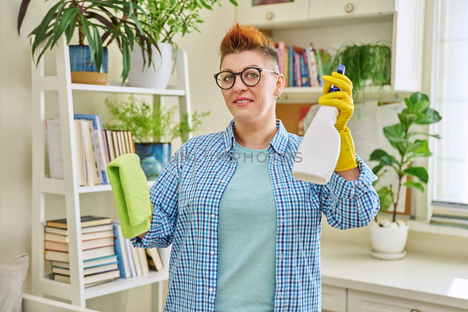 Middle-aged woman cleaning house, female looking at camera, wiping dust in room. Housekeeping, housework, housecleaning, cleaning concept