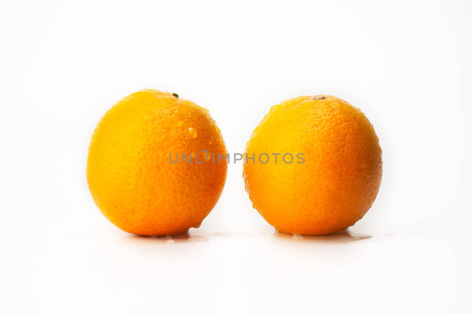Two oranges are sitting on a white background. The oranges are wet and shiny. Concept of freshness and vitality