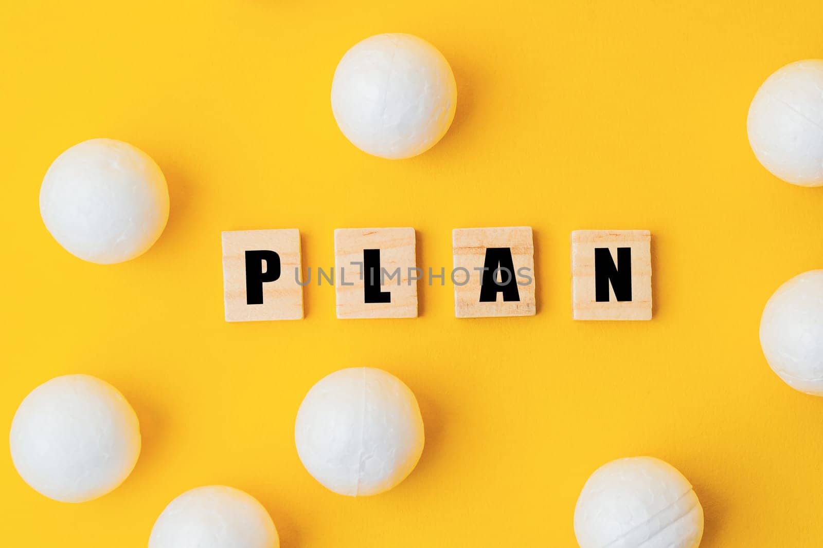 A yellow background with a large group of white balls scattered around it. The word plan is written in black letters on top of the balls, creating a playful and creative atmosphere