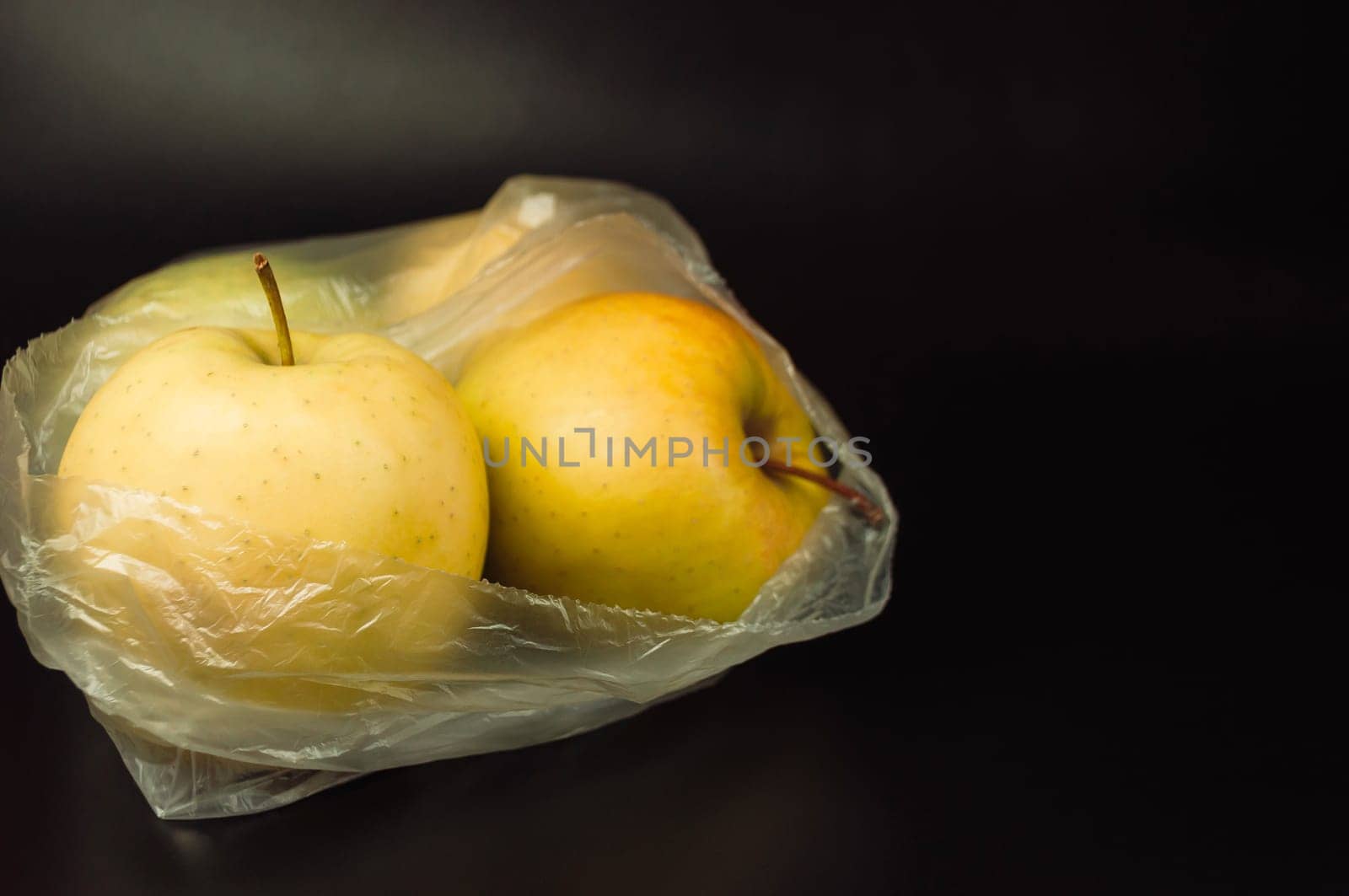 A plastic bag with two apples in it. Fresh apples, encased in non-recyclable plastic