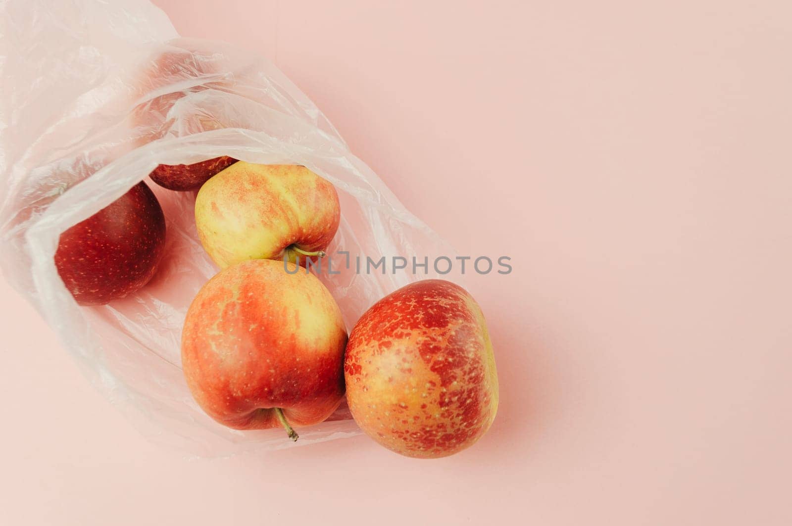 A bag of apples is on a pink background. The apples are red and green