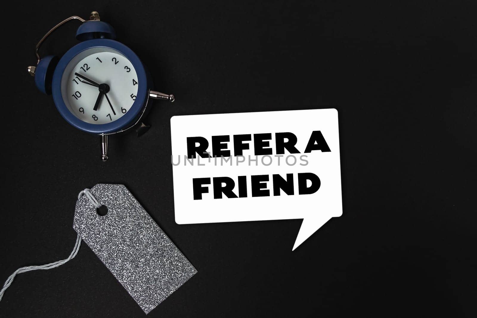 A clock sits on a table with a tag that says refer a friend. The clock is blue and white and has a black face