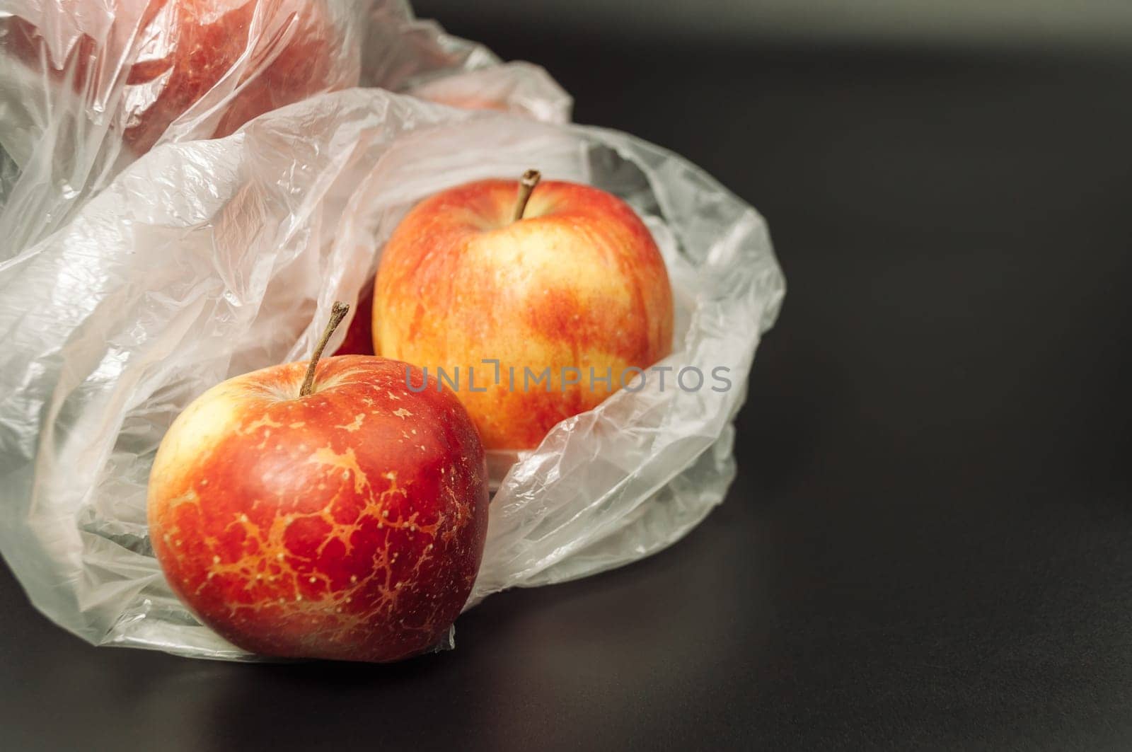 Two apples are in a plastic bag on a black background. The apples are red and shiny