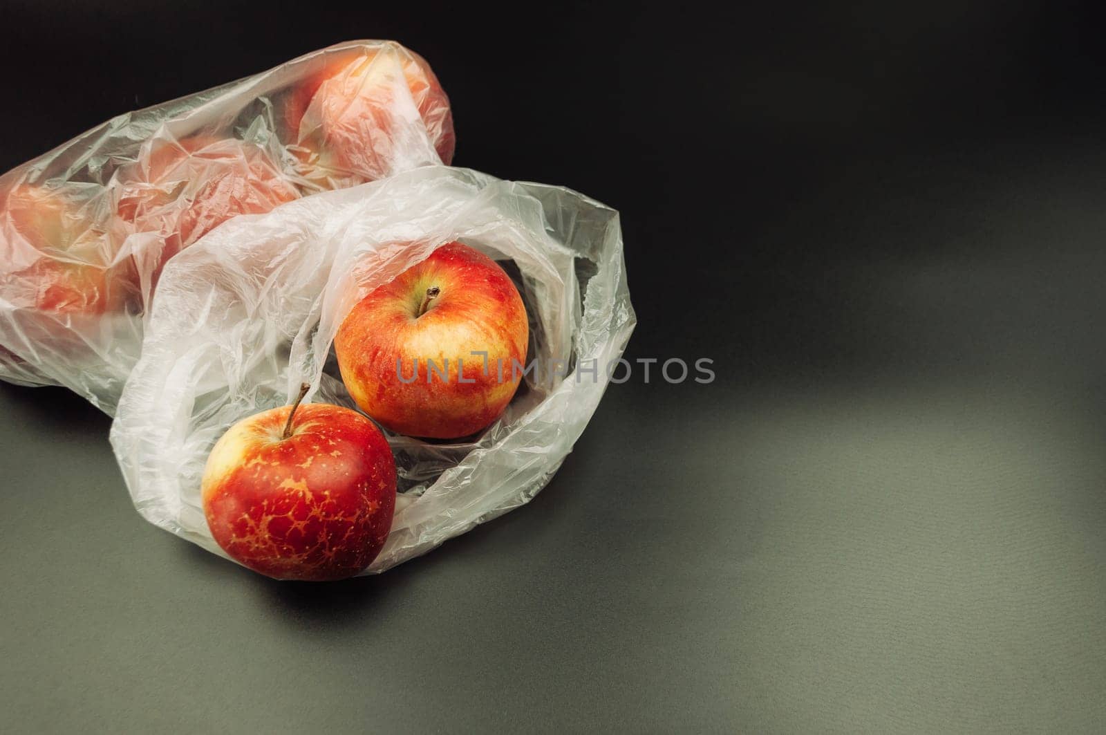 A bag of apples is sitting on a black background. The apples are red and have a few brown spots. The bag is made of plastic and is open
