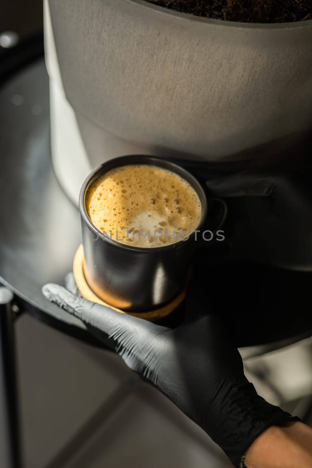 Close-up of a human hands in black gloves holding and showing a cup with a hot drink. The doctor poured coffee from the coffee machine