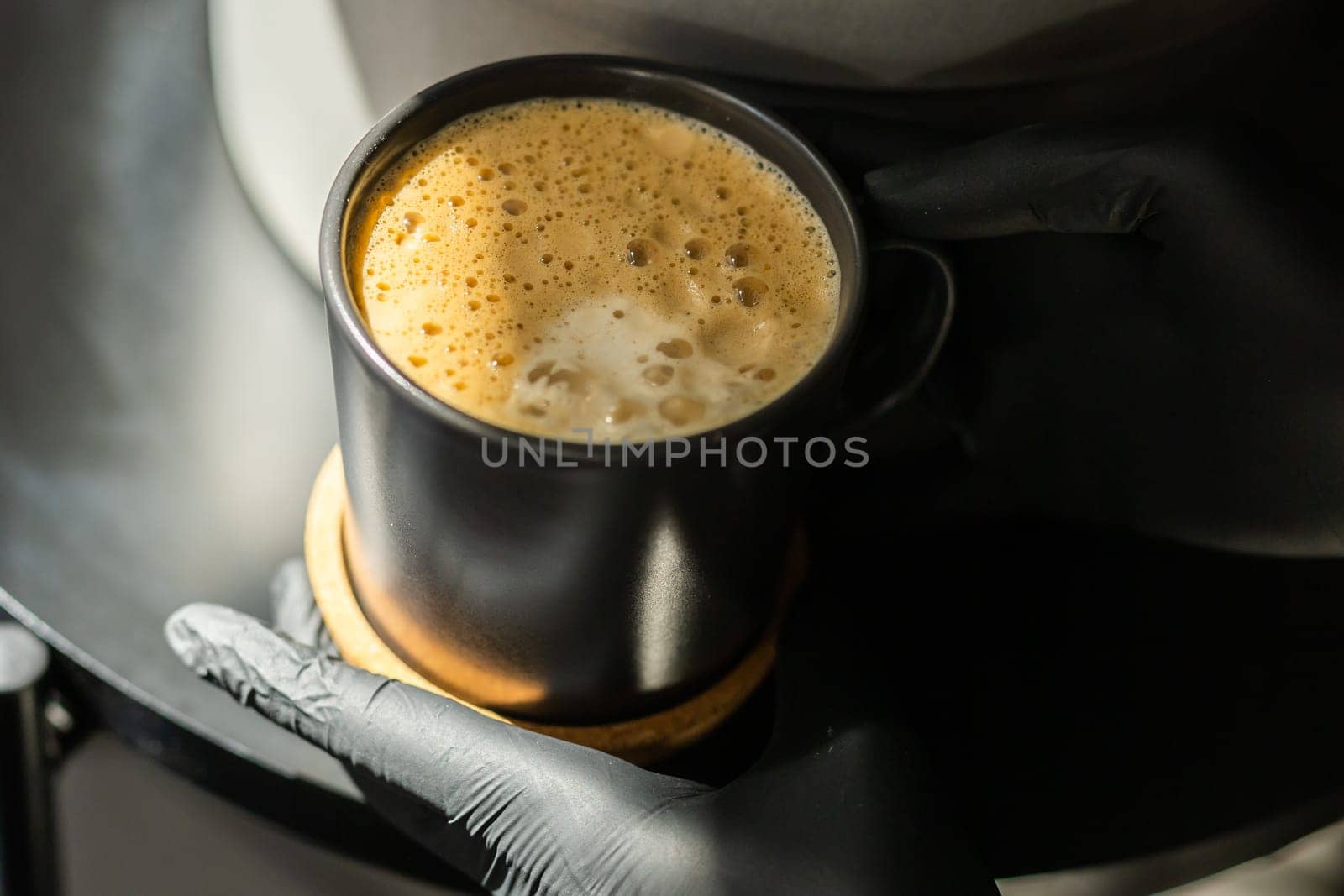 Close-up of a human hands in black gloves holding and showing a cup with a hot drink. The doctor poured coffee from the coffee machine. by Satura86