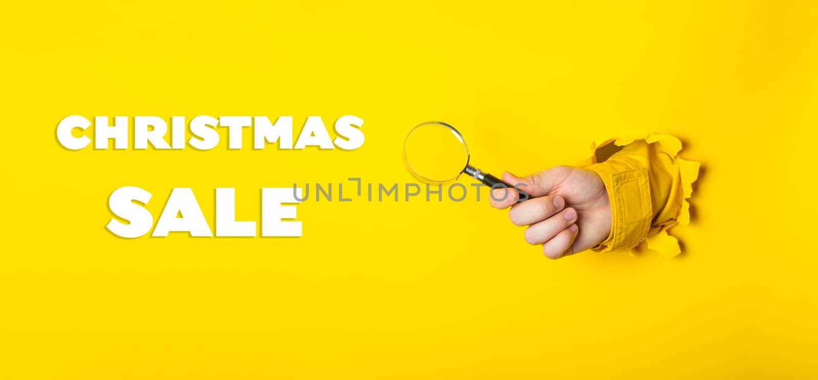 A person holding a magnifying glass with the words Christmas Sale written below. The image has a festive and playful mood