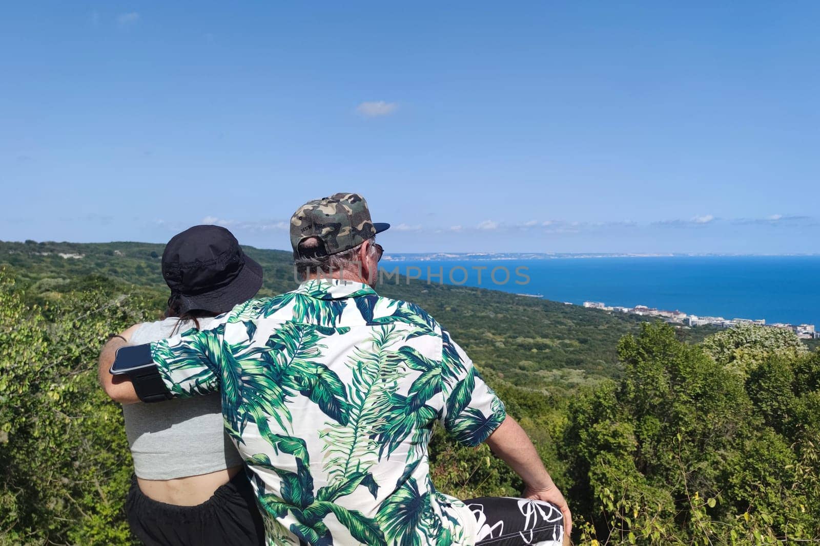 dad and teenage girl sitting on the mountain and looking at the sea horizon, rear view by Annado