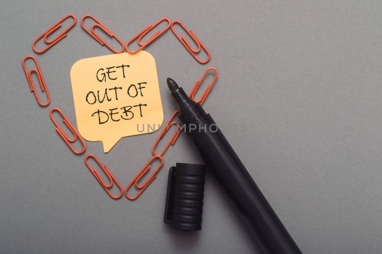 A pen with a note on it that says Get out of debt. The note is surrounded by paper clips, creating a heart shape. Concept of overcoming financial struggles and taking control of one's finances