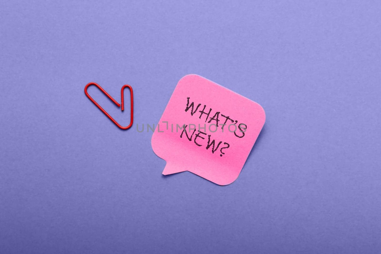 A red clip is on a pink piece of paper that says What's new. The clip is on the left side of the paper and the paper is on a blue background