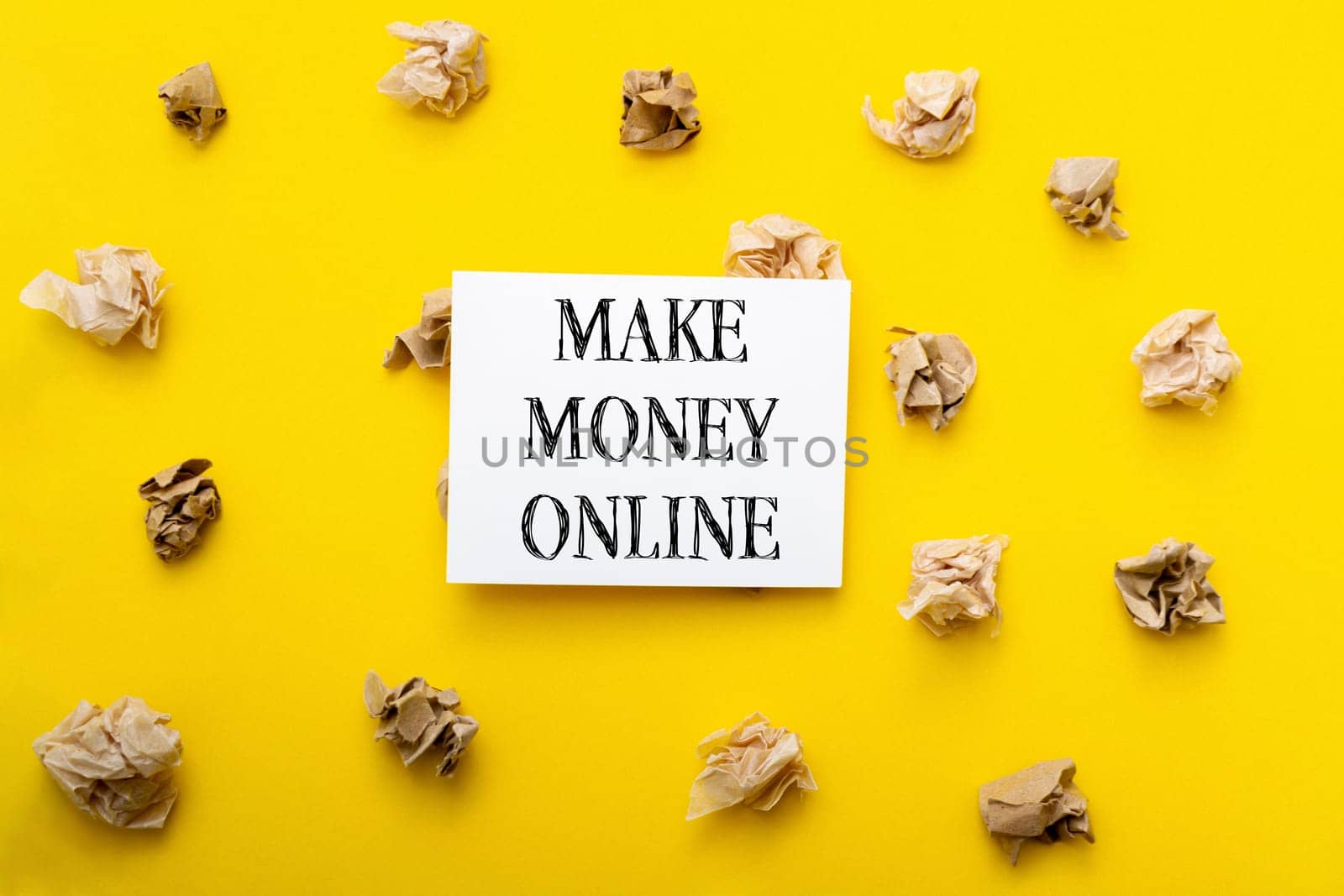 A white sign with the words Make Money Online written on it is placed on top of a yellow background. The sign is surrounded by crumpled paper, giving the impression of a cluttered