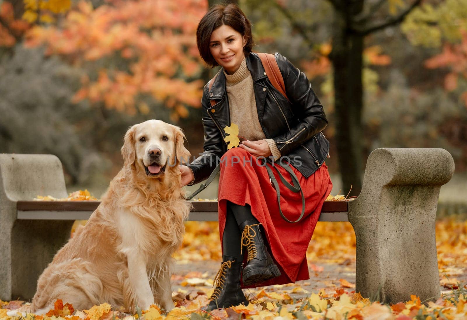 Woman sitting on a bench in an autumn park and petting a Golden Retriever dog by tan4ikk1