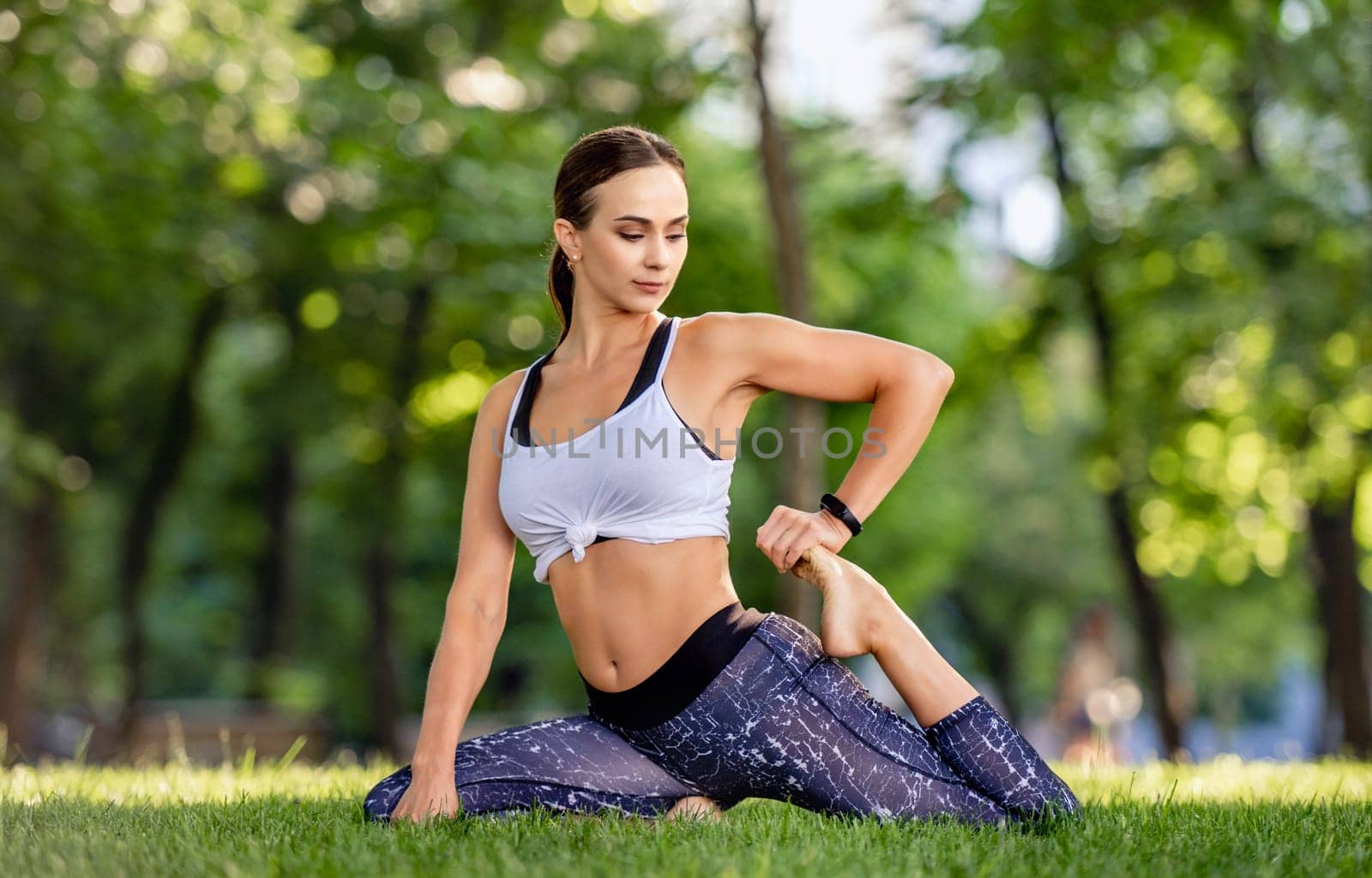 Beautiful girl during yoga workout at the nature stretching her legs. Young woman doing fitness exercises