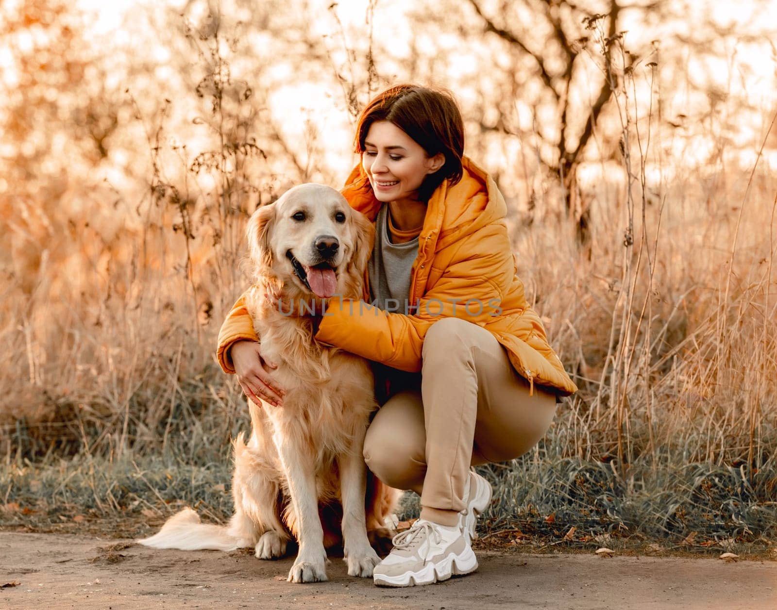 Girl hugging golden retriever dog with sunset light outdoors. Young woman petting doggy pet labrador at nature at autumn